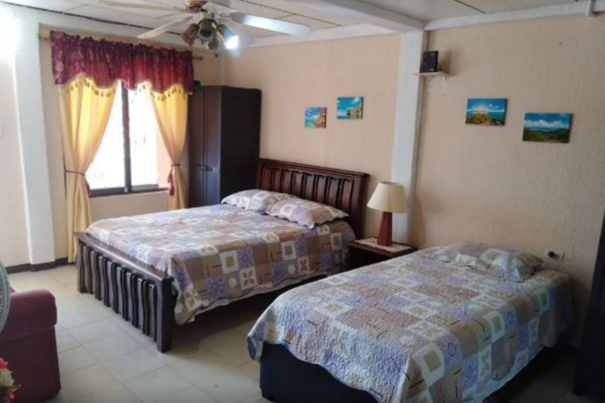 Une chambre avec deux lits, un ventilateur de plafond et une fenêtre avec des rideaux.