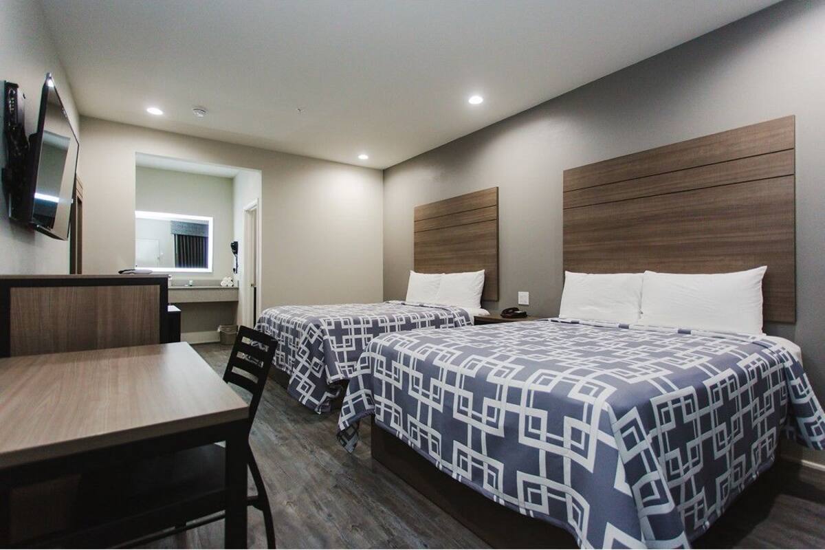 A hotel room with two beds, a desk, a chair, a TV, and a bathroom visible through an open door.
