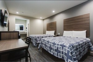 Habitación de hotel con dos camas, un escritorio, una silla, un televisor y un baño visible a través de una puerta abierta.