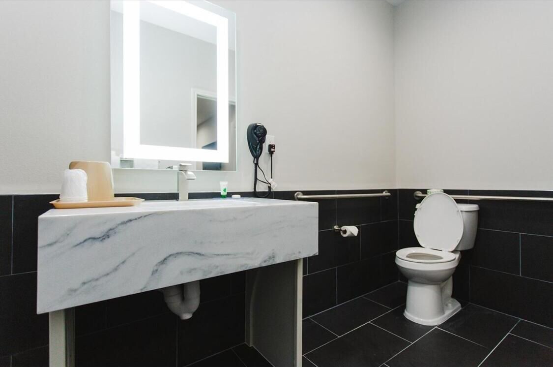 Un baño moderno con lavamanos de mármol, un espejo grande, un secador de pelo y un inodoro.