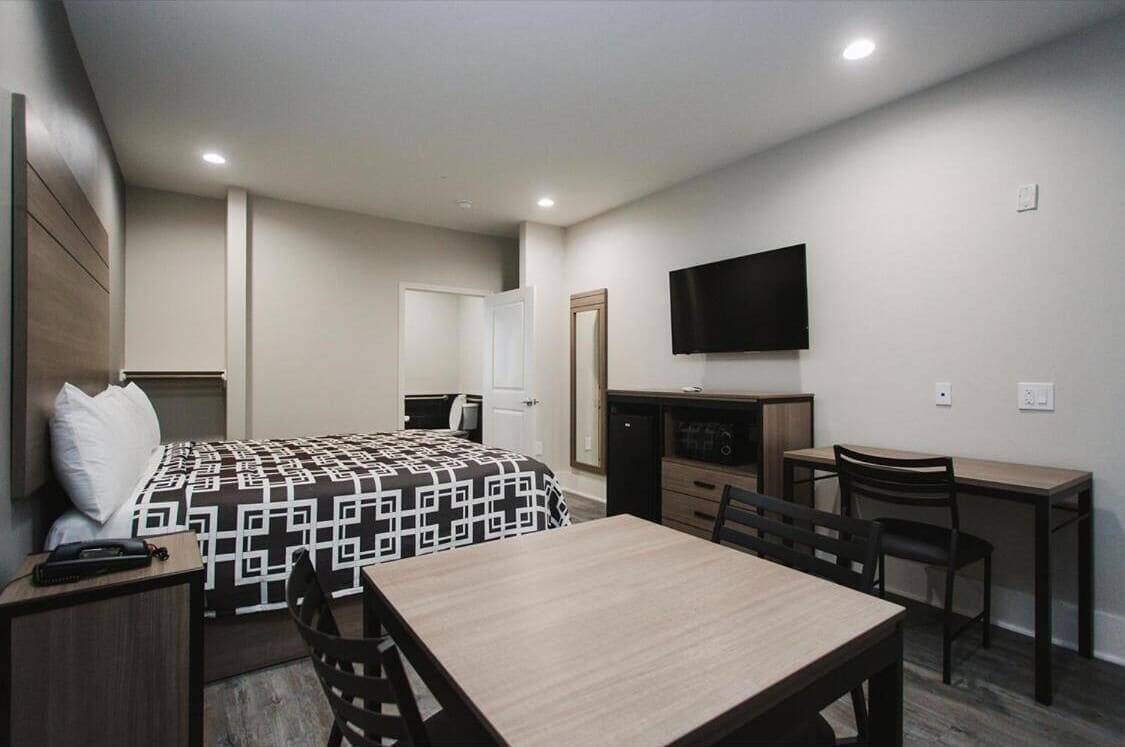 A hotel room with a bed, a desk, a chair, a television, and a wardrobe.