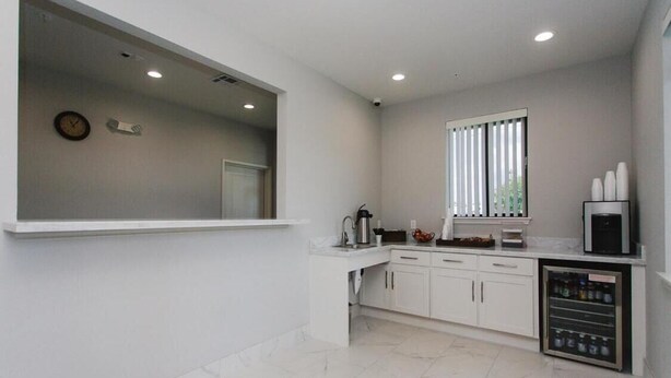 A modern kitchen with white cabinets, a built-in microwave, and a window with blinds. - Palace Inn Conroe (Conroe)
