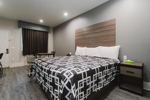 A modern hotel room with a large bed, a wooden headboard, a bedside table, and a chair.