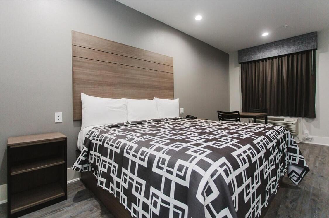 A modern hotel room with a large bed, a wooden headboard, a small table, and a chair.