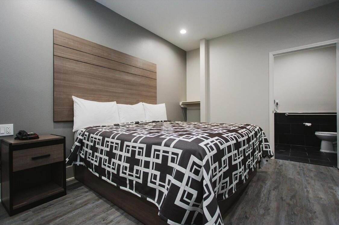 A modern bedroom with a large bed, a nightstand, a wooden headboard, and a bathroom with a toilet and sink.