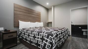 A modern bedroom with a large bed, a nightstand, a wooden headboard, and a bathroom with a toilet and sink.