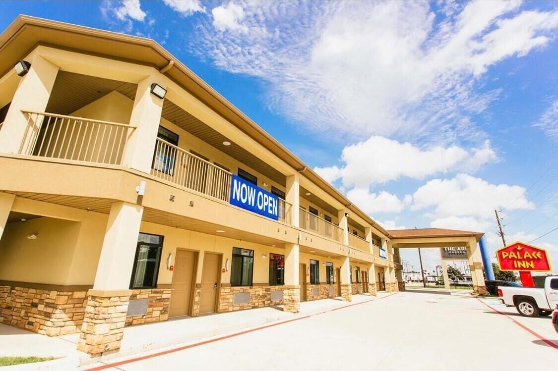 A hotel with a 'NOW OPEN' sign, a balcony, and a 'PALACE INN' sign.