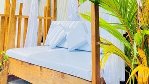Un lit en bois avec du linge de lit blanc, une structure de plafond en bois et une plante en pot.