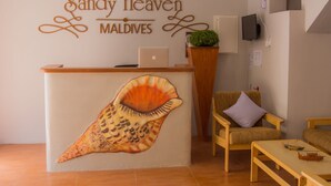 Un comptoir d’accueil orné d’une fresque représentant des coquillages, un ordinateur portable, une plante et un espace détente avec une table et des chaises en bois.