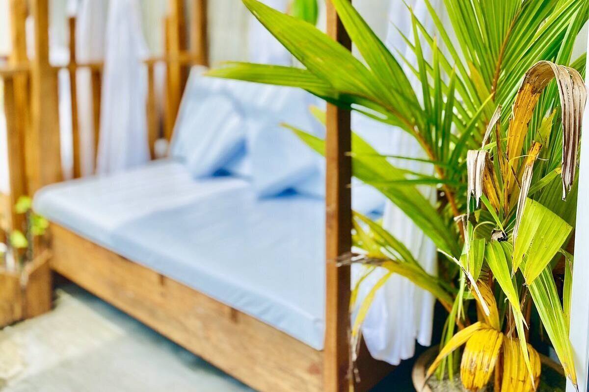 A single bed with a wooden frame and white curtains in a room with a thatched roof.