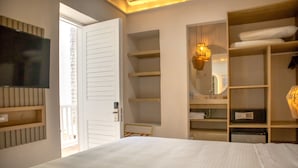 Une chambre d’hôtel avec un lit, un téléviseur fixé au mur, une armoire et une étagère avec des serviettes.