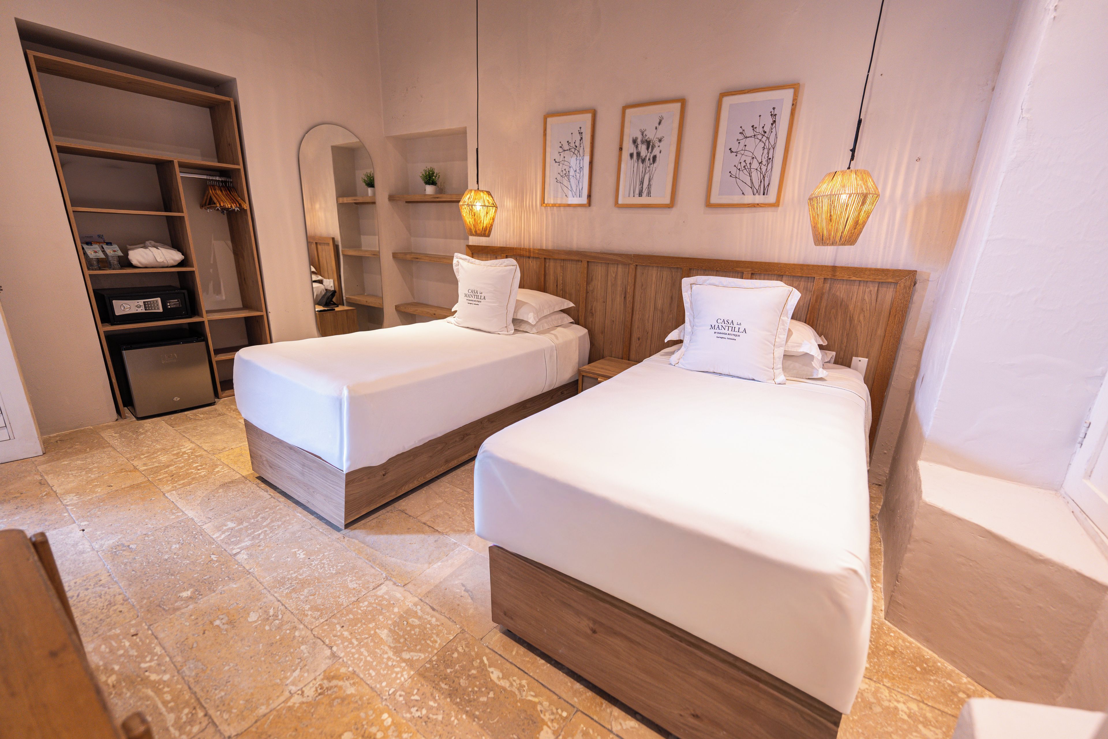 Habitación de hotel con dos camas, un armario, un espejo y cuadros en la pared.
