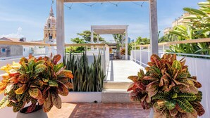 Un espace extérieur abrité, doté d’une pergola, de plantes en pot et offrant une vue sur le clocher d’une église.
