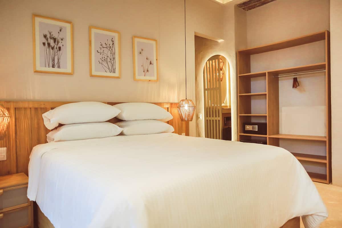 Een net opgemaakt bed met witte lakens, een houten hoofdbord en een wandplank met een hangend object.