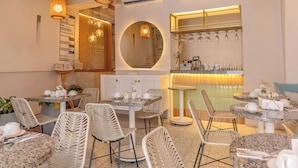 Un restaurant avec des chaises en osier, des tables rondes et des luminaires suspendus.