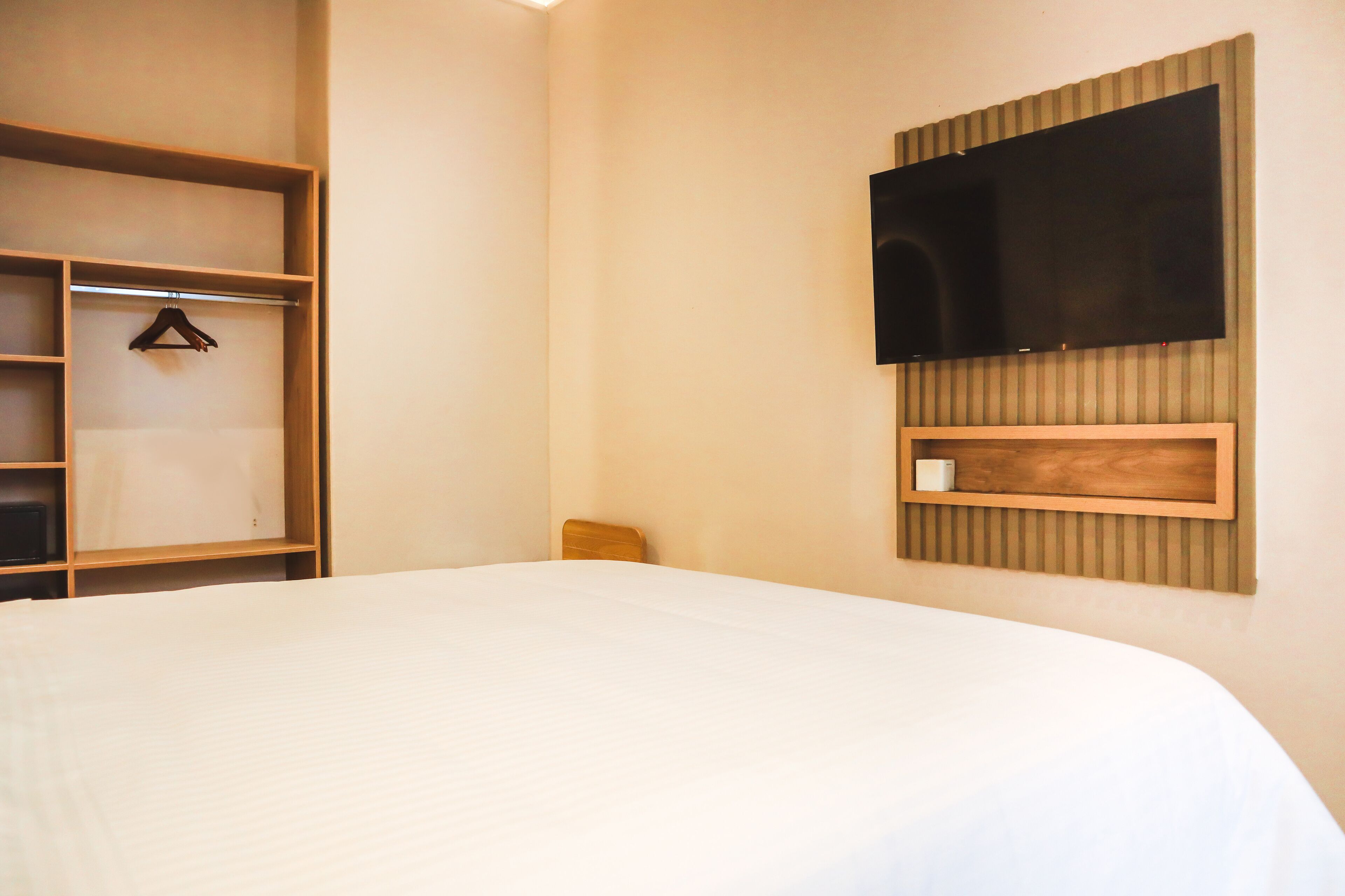 Ein Hotelzimmer mit einem Bett, einem Holzschrank, einem an der Wand befestigten Fernseher und einer kleinen Holzkabine unter dem Fernseher.