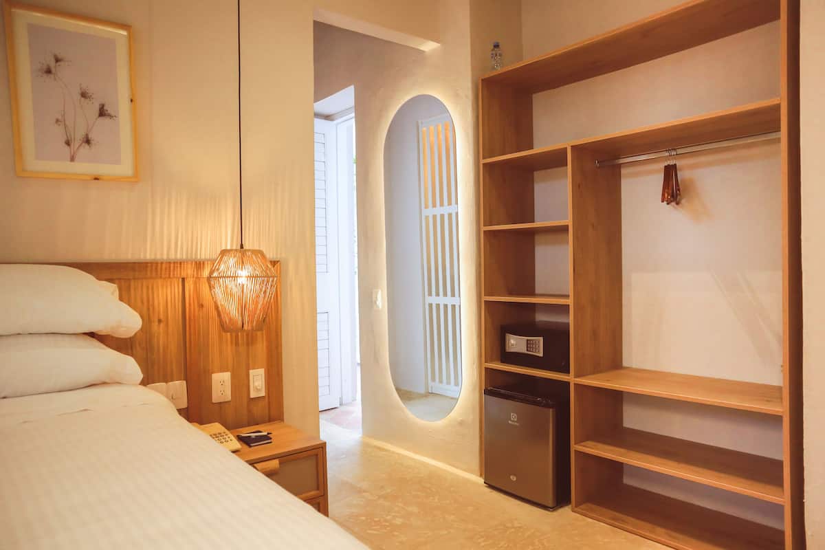 Een hotelkamer met een bed, nachtkastje, bureau, spiegel, kledingkast en een kleine koelkast.