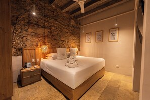 A bedroom with a stone wall, a wooden bed frame, a nightstand with a phone, and three framed pictures on the wall.