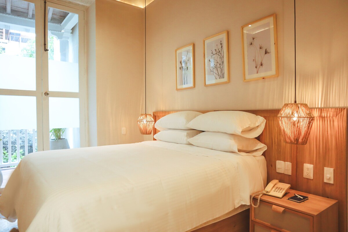 A hotel room with a large bed, bedside lamps, a nightstand with a phone, and framed artwork on the wall.