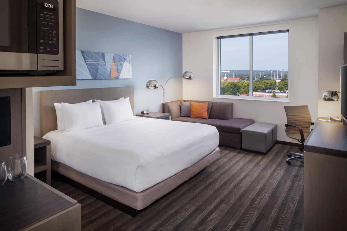 A modern hotel room with a large bed, a desk, a chair, and a window with a city view.