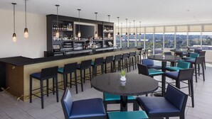A modern bar area with a long counter, multiple seating options, and a view of the cityscape. - Hyatt House Augusta Downtown (Augusta)