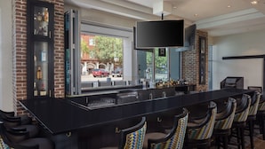 A bar area with a long counter, multiple stools, and a television mounted above. - Hyatt House Augusta Downtown (Augusta)