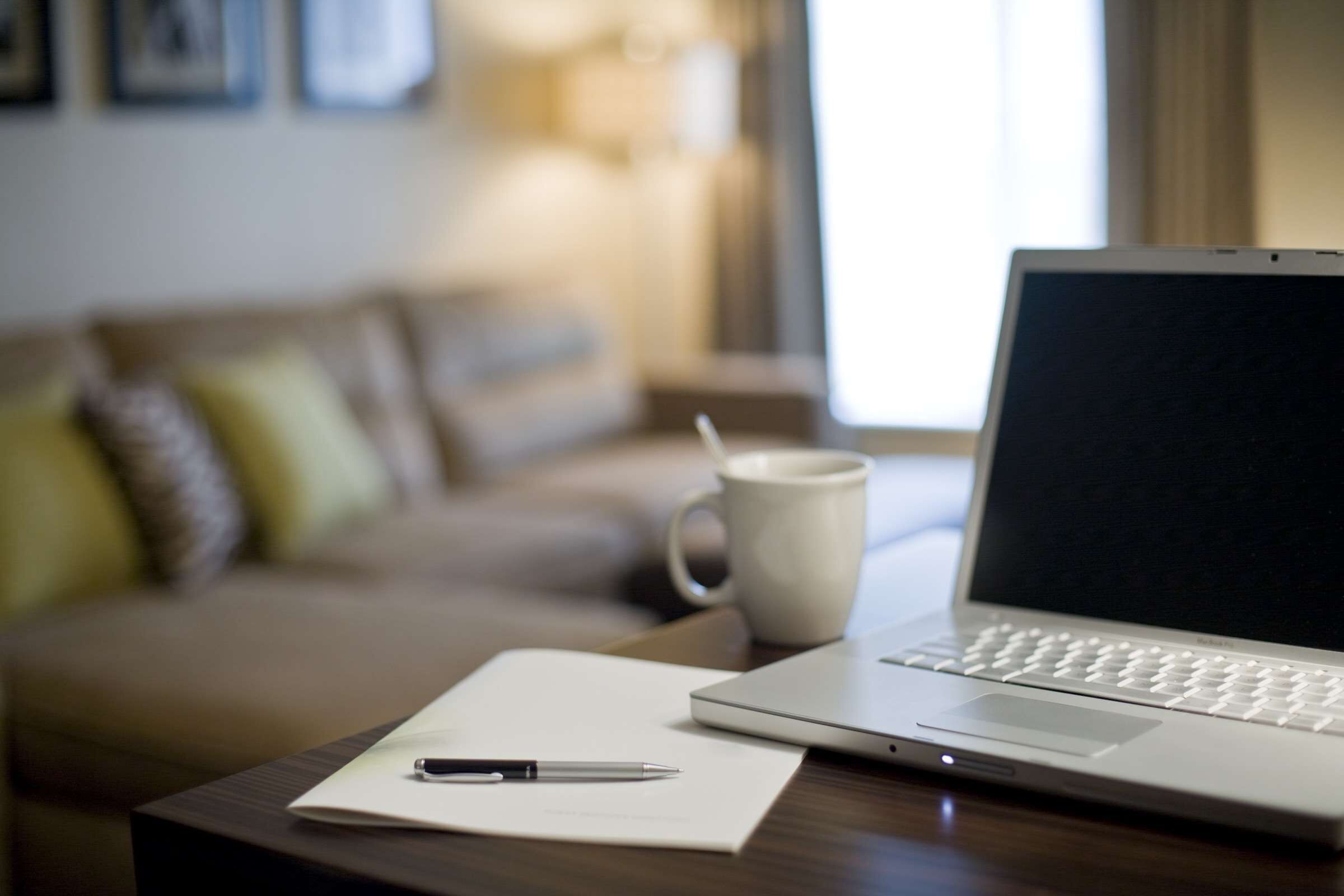 A laptop on a wooden table with a white mug and a pen on a piece of paper.