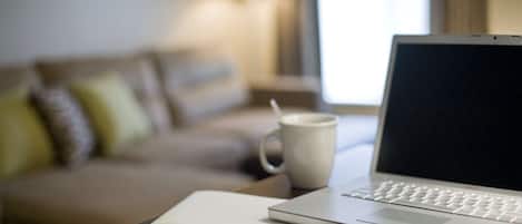 A laptop on a wooden table with a white mug and a pen on a piece of paper.