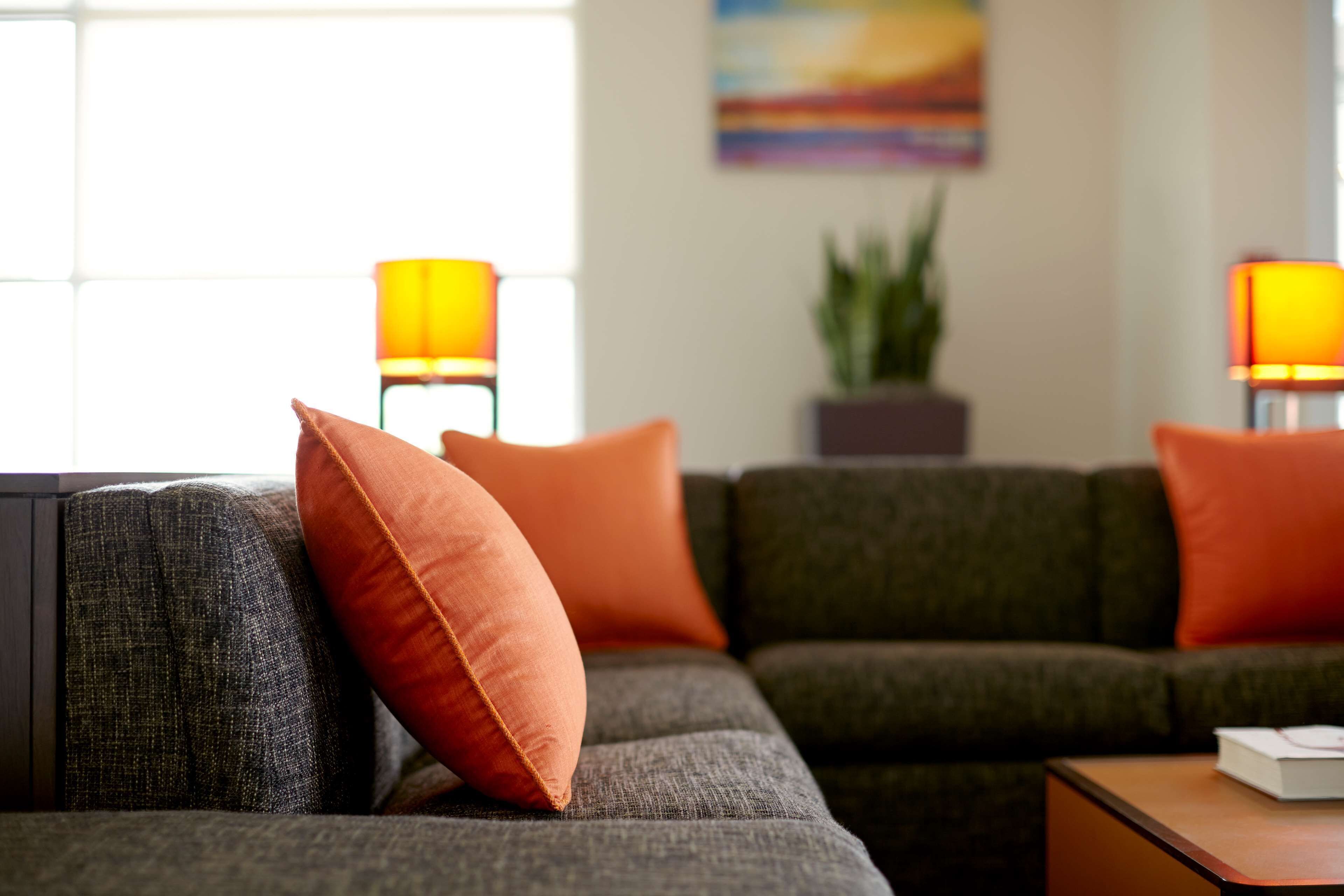 A modern living room with a grey sofa, orange cushions, and two floor lamps.