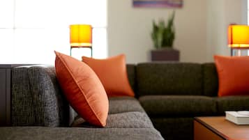 A modern living room with a grey sofa, orange cushions, and two floor lamps.