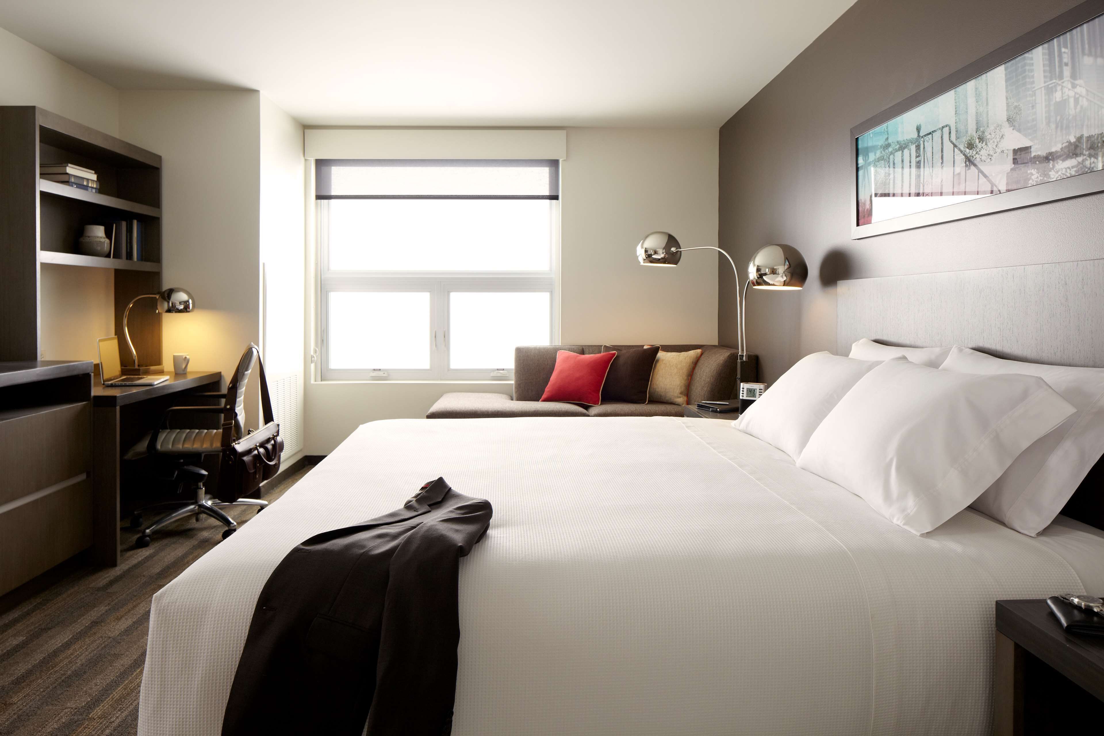 Une chambre d’hôtel avec un grand lit, un bureau, une chaise, une bibliothèque et une fenêtre.
