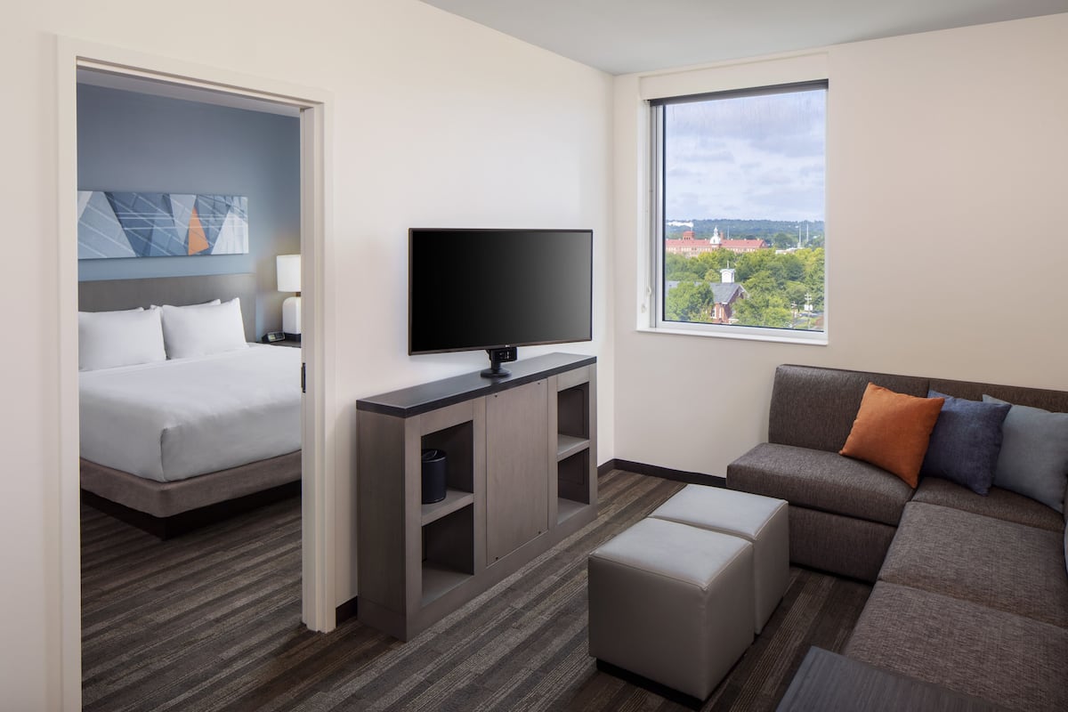 A hotel room with a bed, a TV, a sofa, and a window with a city view.