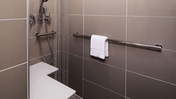 A shower area with a white bench, a grab bar, and a towel rack. - Hyatt House Augusta Downtown (Augusta)