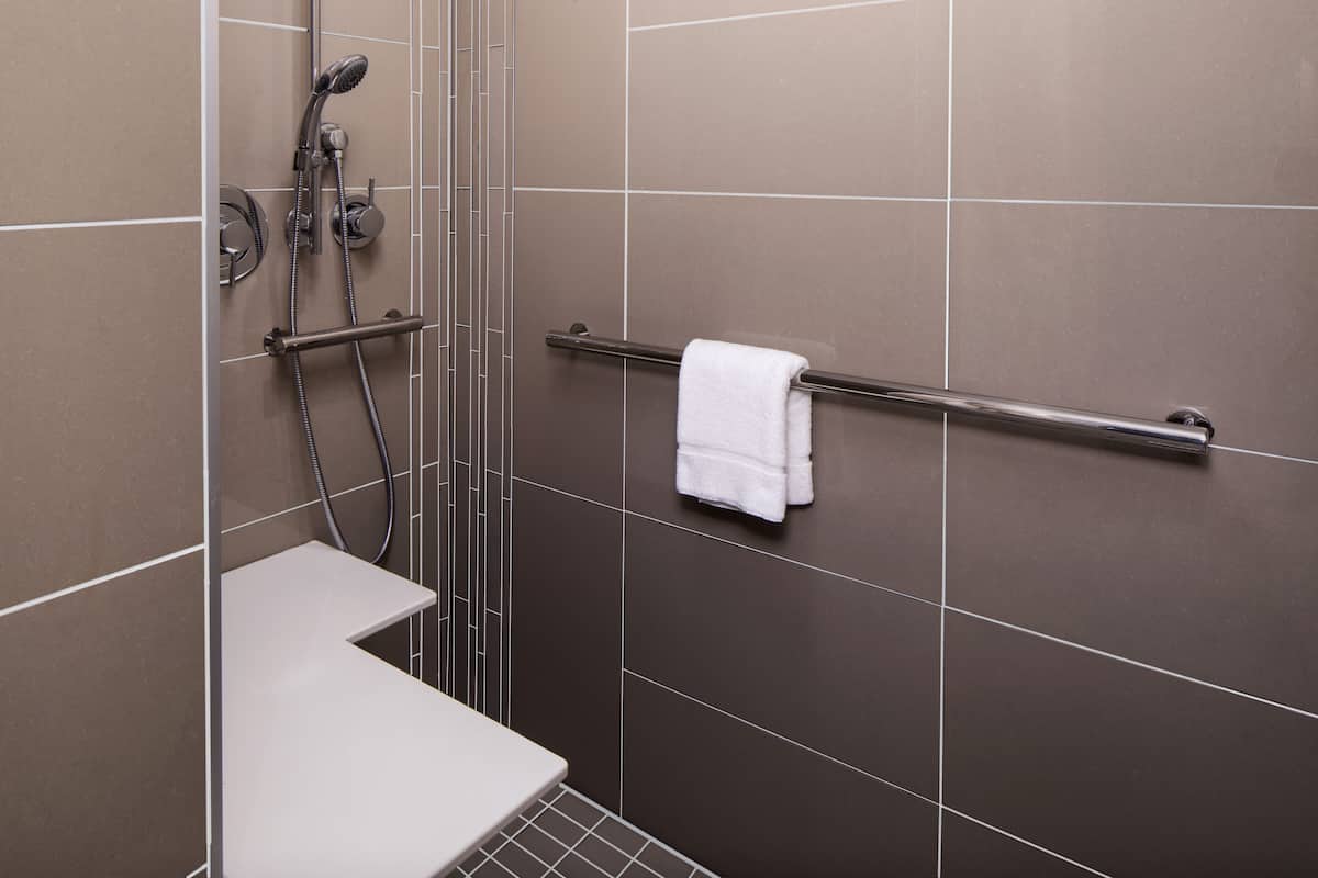 A shower area with a white bench, a grab bar, and a towel rack.