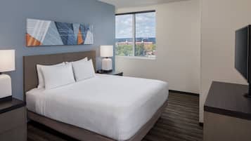 Quarto de hotel com uma cama grande, duas mesas de cabeceira com luminárias, uma TV de tela plana e uma janela com vista para a cidade.