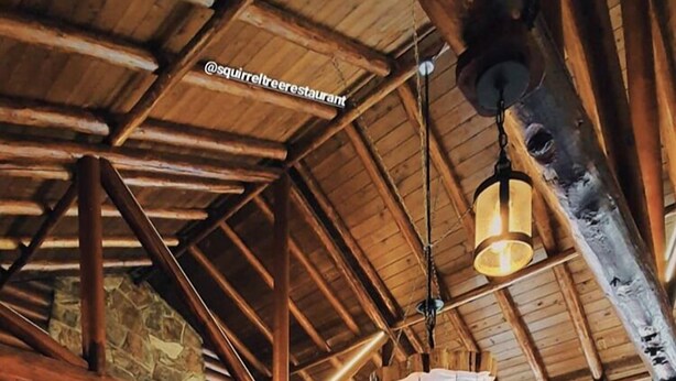 Un interior rústico de madera con paredes de piedra, mesas y sillas de madera, y una chimenea de piedra.