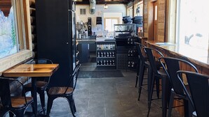 Un interior rústico con vigas de madera, suelo de piedra y una zona de bar con taburetes y mostrador.