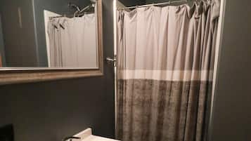 Um banheiro com pia branca, armários escuros, um espelho e um cortinado de chuveiro.