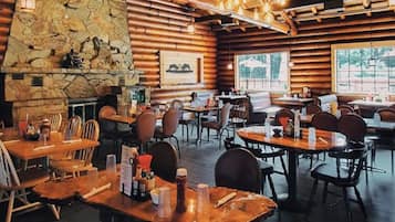 A rustic wooden interior with stone walls, wooden tables and chairs, and a stone fireplace.