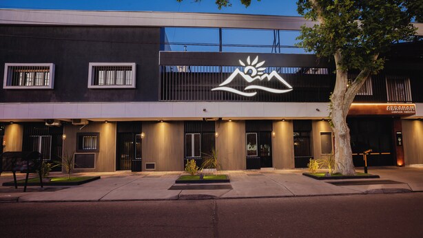 A modern hotel facade with a mountain and sun logo, large windows, and a well-lit entrance.