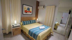 A hotel room with a bed, bedside tables, a nightstand, a wall-mounted air conditioner, and a framed picture.