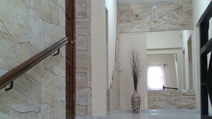 A staircase with stone walls and a wooden handrail leading to a room with a white door and a vase on a table.
