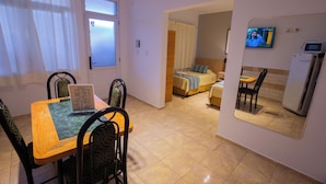A hotel room with a dining area, a bed, a TV, and a kitchen area.