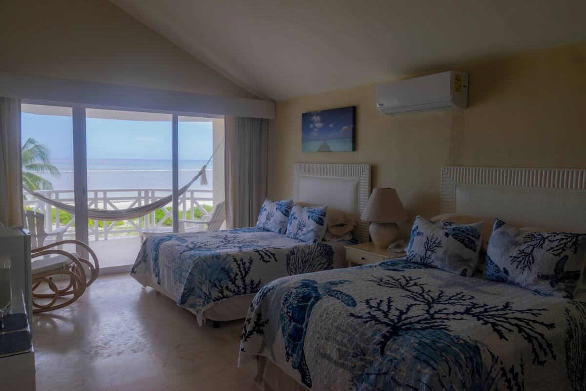 Una habitación de hotel con dos camas, vista al océano, una hamaca y un ventilador de techo.