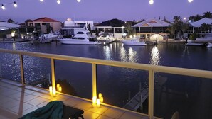 Un puerto deportivo al anochecer, con barcos amarrados, un balcón con vistas al agua y luces colgantes.
