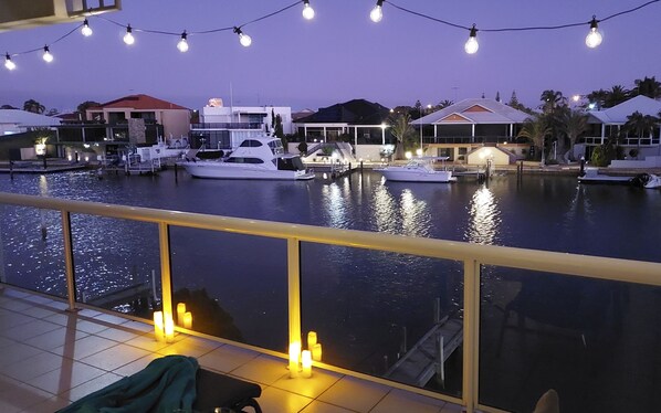 A marina at dusk with boats docked, a balcony with a view of the water, and string lights above.