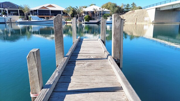 Un muelle de madera que da a un puerto deportivo con barcos y edificios al fondo.