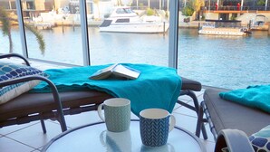 Vista desde un balcón con una mesa, dos tazas estampadas y un libro sobre una manta color turquesa.
