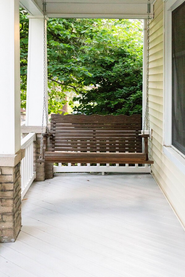 A porch with a wooden bench, white railings, and a view of greenery.