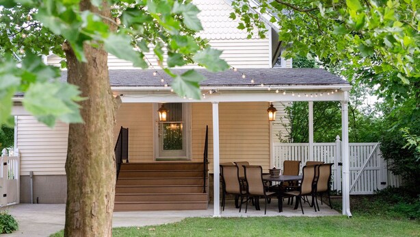 Une terrasse couverte avec une table et des chaises, un escalier en bois et une clôture blanche.